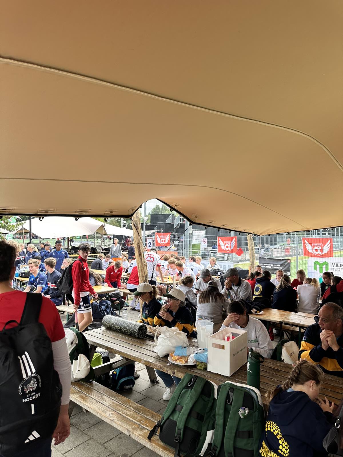 Teams uit binnen- en buitenland aan de picknicktafels onder de overkapping bij het clubhuis van Athena