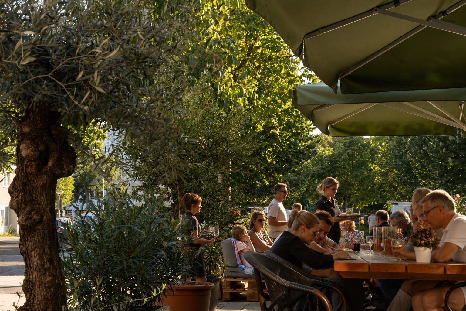 Bediening loopt met borden langs een lange tafel op het terras van Brasserie Lenny in de avondzon