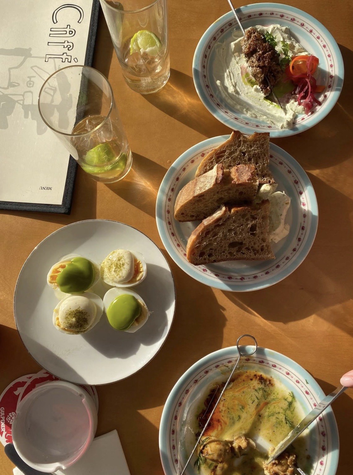 Verschillende gerechten van Café Publiek op tafel in de avondzon, met brood, salades en drankjes