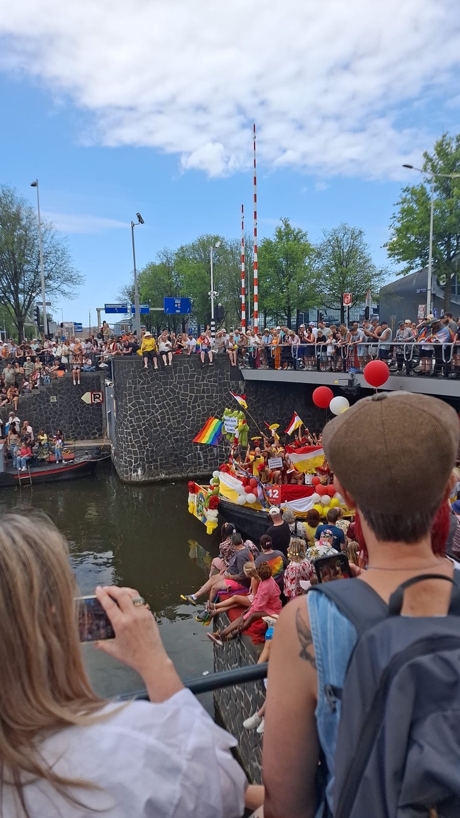 Publiek met ballonnen kijkt vanaf een brug naar een versierde boot tijdens de Canal Parade