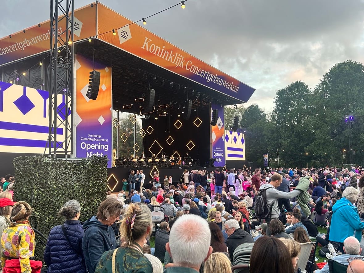 Het podium van het Koninklijk Concertgebouworkest bij schemering, met publiek verspreid over het gras
