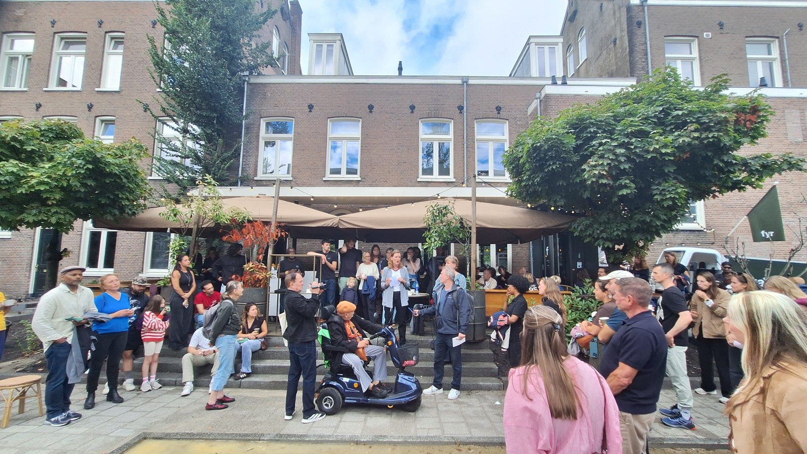 Stadsdeelvoorzitter Amélie Strens spreekt een groep buurtbewoners en ondernemers toe bij het terras van restaurant FYR