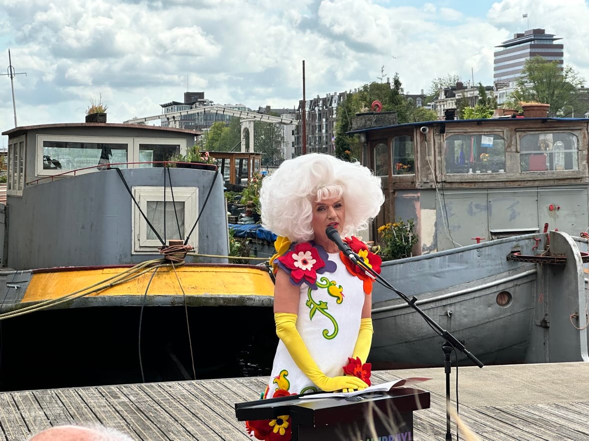 Dolly Bellefleur spreekt de gasten toe vanaf de steiger bij het H'ART Museum, met woonboten op de Amstel op de achtergrond