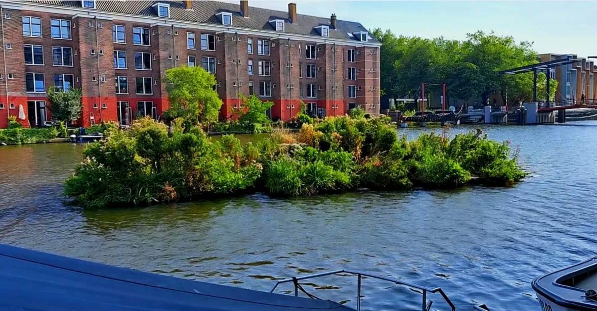 Een drijvende tuin in de Wittenburgervaart met groen begroeide eilanden voor de rood-bruine gevels van Oostenburg