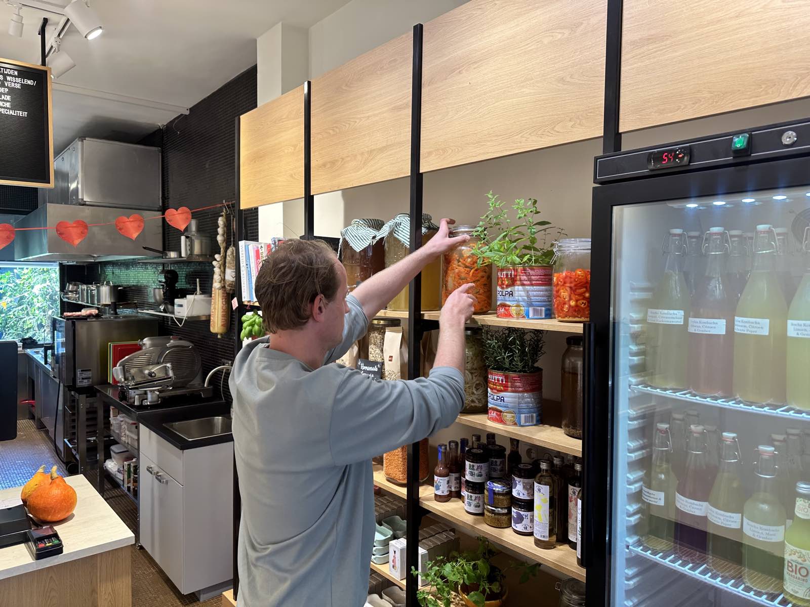 Koen van Keulen reikt naar potten met zelfgemaakte kimchi en kombucha op een schap vol delicatessen