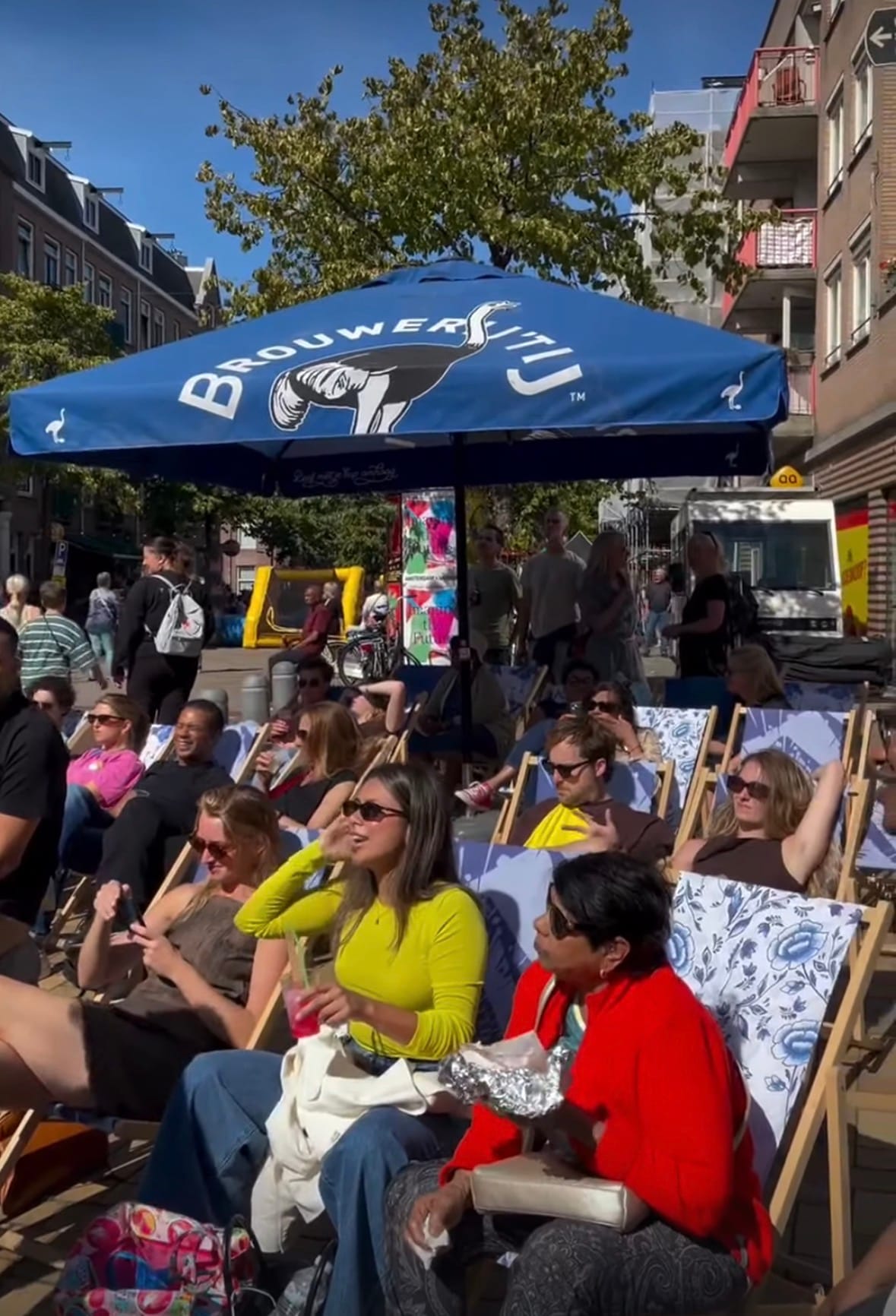 Bezoekers ontspannen in ligstoelen onder een parasol van Brouwerij ’t IJ tijdens het festival