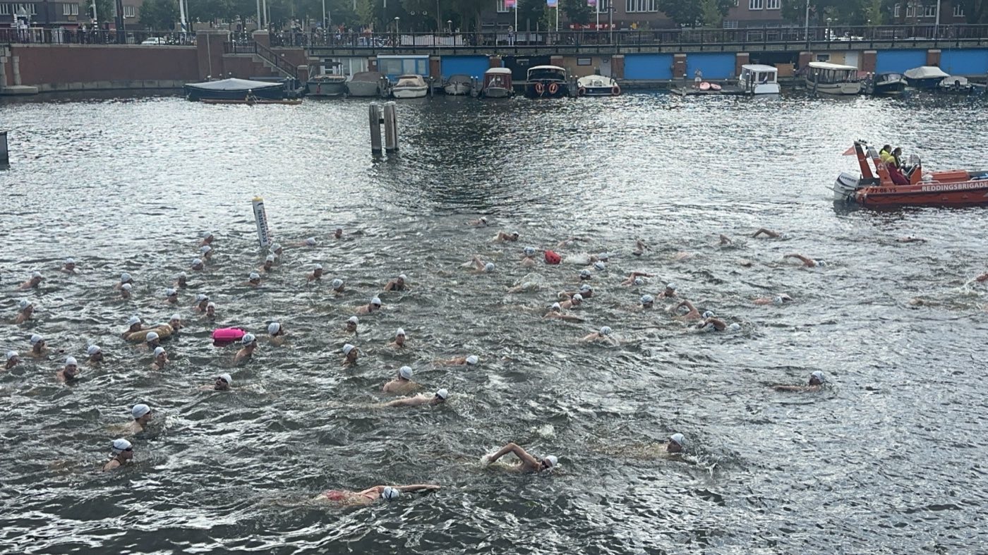 Zwemmers van LoveSwim in de Amstel, met de reddingsboot van de veiligheidsbrigade op de uitkijk