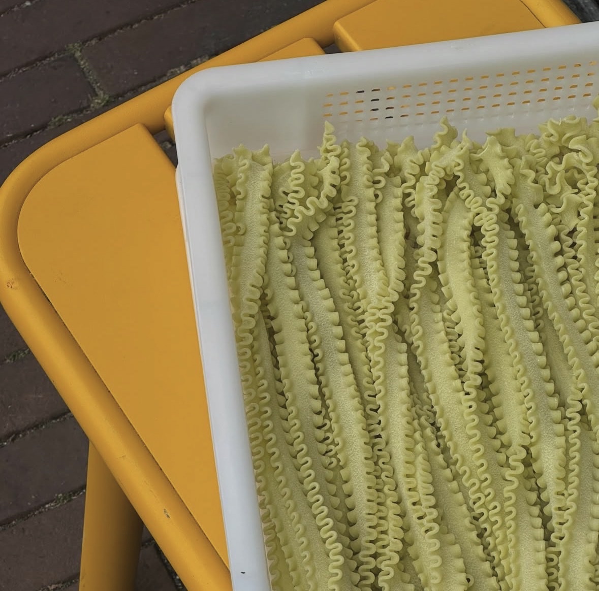 Bakken met vers gedraaide pasta die buiten op een gele stoel liggen te drogen