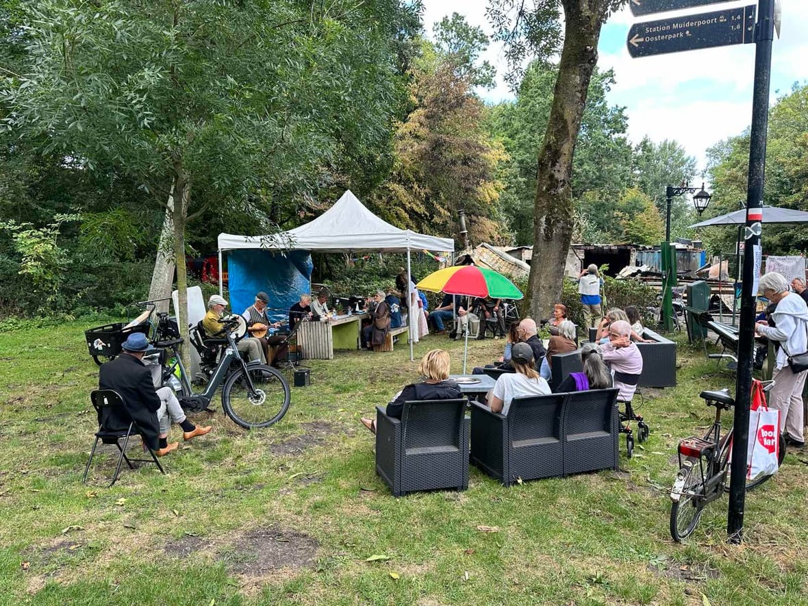 Bezoekers van Parknest zitten met livemuziek naast de uitgebrande ruïne in het Flevopark