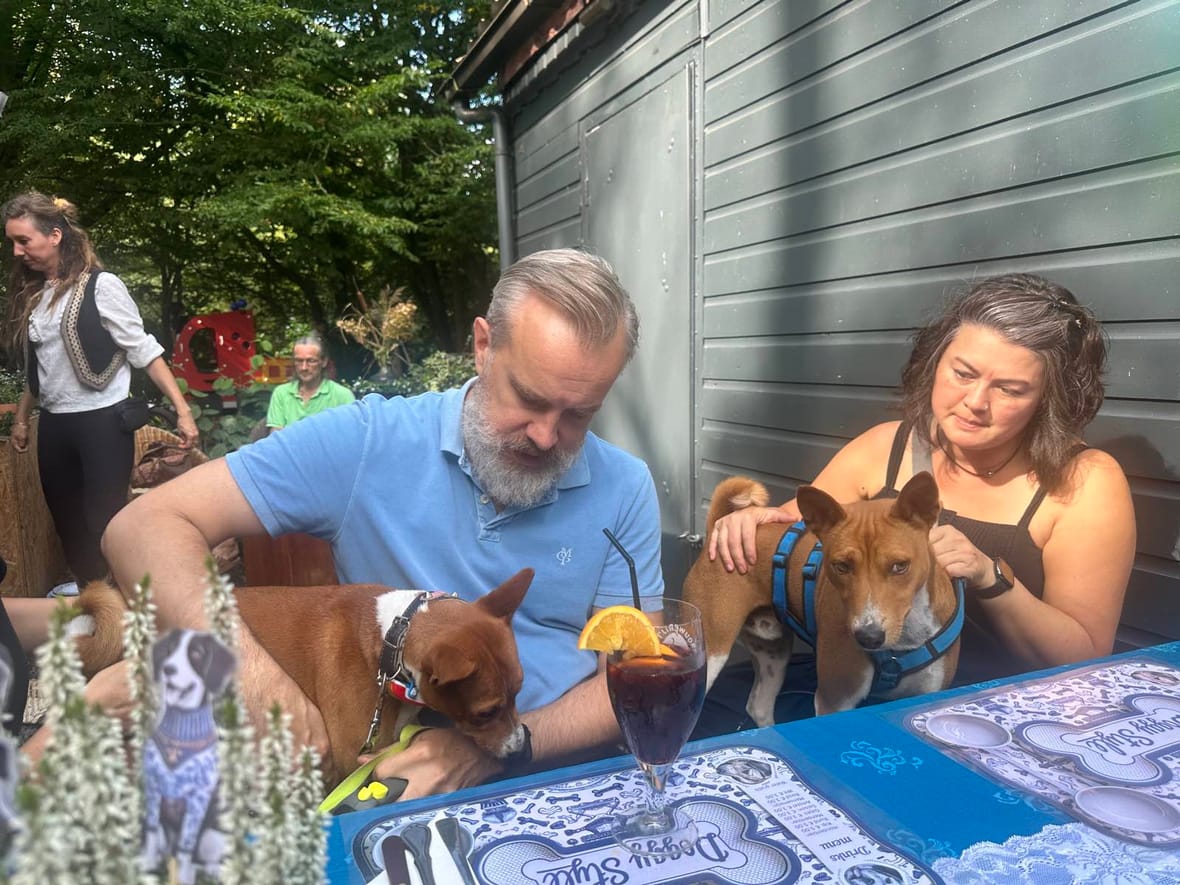 Twee honden aan tafel bij hun baasjes, met voor hen de placemats van het Doggy Style-menu