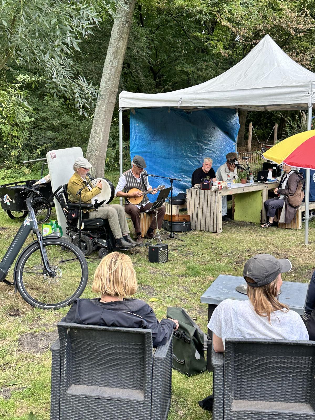 Twee muzikanten spelen onder een tent op bodhrán en mandoline, met toeschouwers op de voorgrond