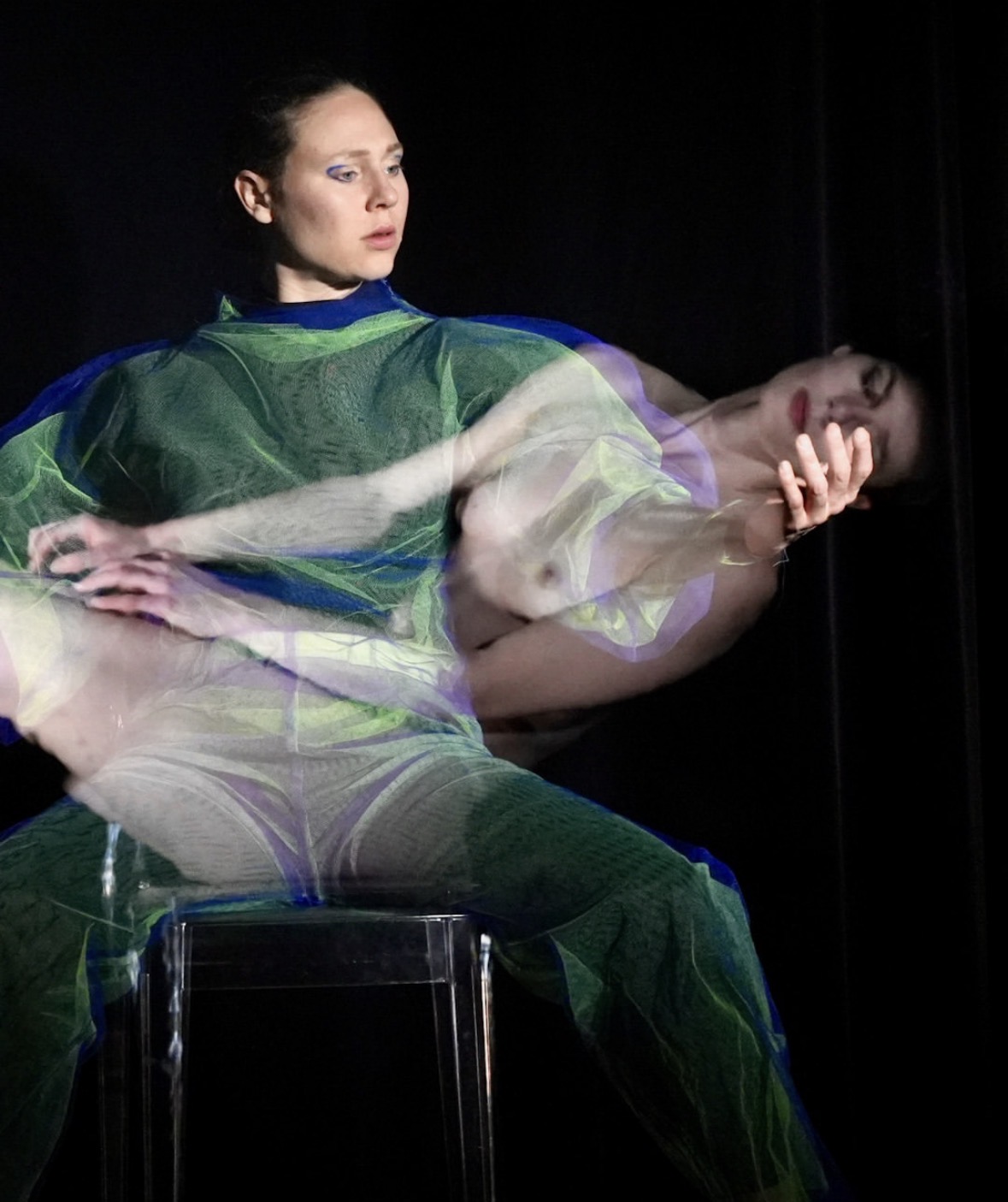 Performer op een kruk, gehuld in doorschijnend groen textiel, tijdens de voorstelling Slug