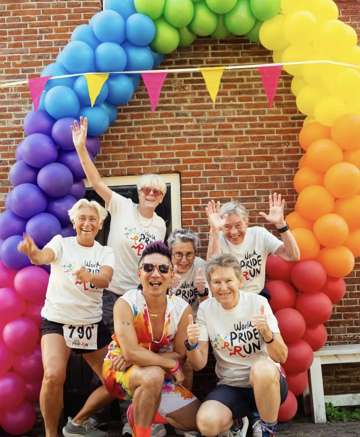 Deelnemers van de Amsterdam Pride Run poseren onder een ballonnenboog in regenboogkleuren (foto: Rainbow Athletics Amsterdam)