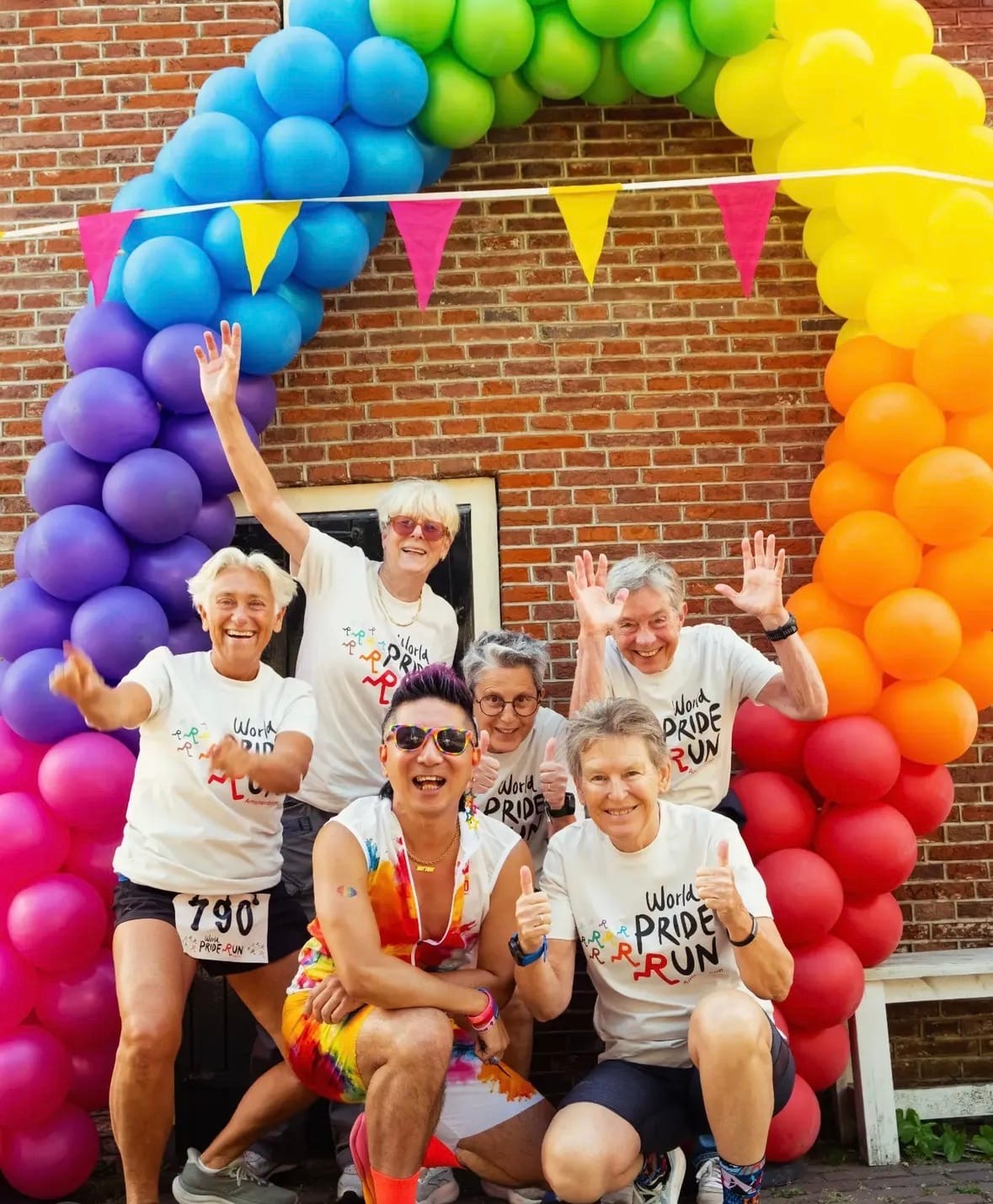Deelnemers van de Amsterdam Pride Run poseren onder een ballonnenboog in regenboogkleuren (foto: Rainbow Athletics Amsterdam)