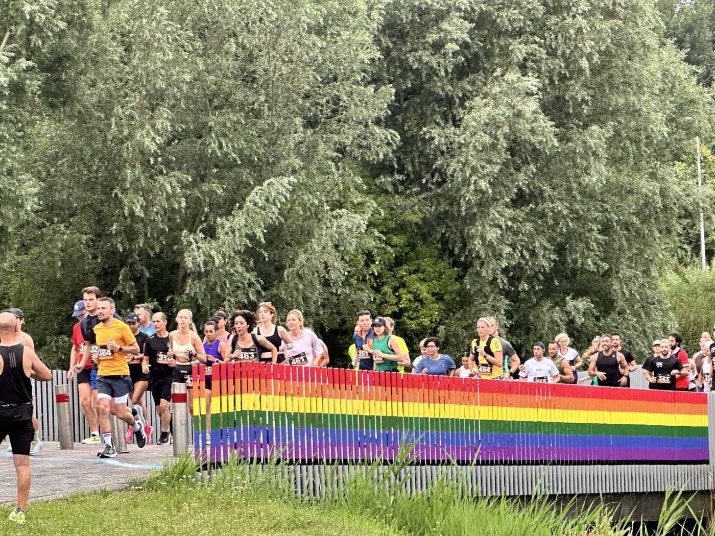 Deelnemers van de Amsterdam Pride Run rennen over een brug met regenboogkleurige leuningen