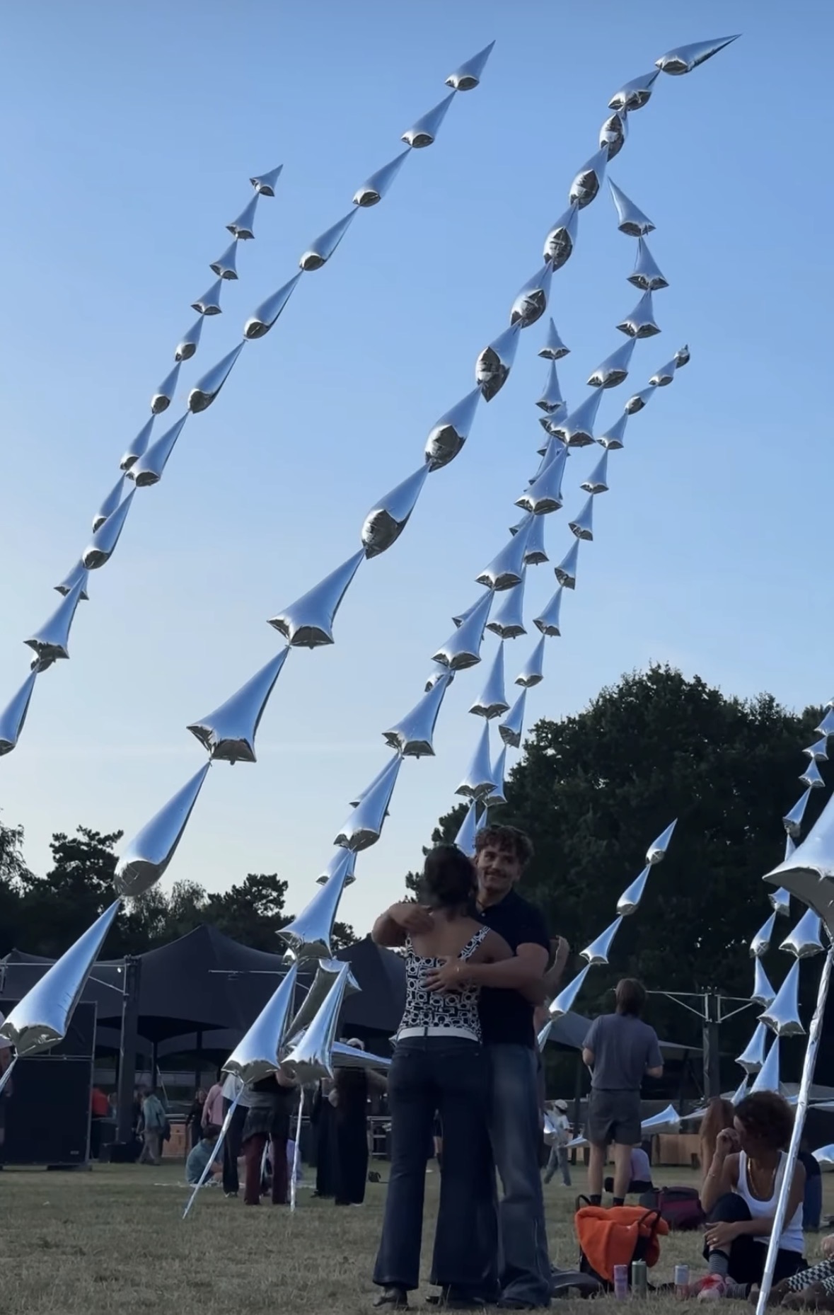 Bezoekers dansen bij zonsondergang tussen de zilverkleurige sculpturen van Steel Grass