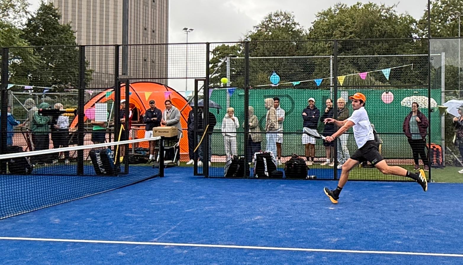 Belangstellenden kijken vanachter het glas toe bij een demonstratiepartij op de nieuwe padelbaan