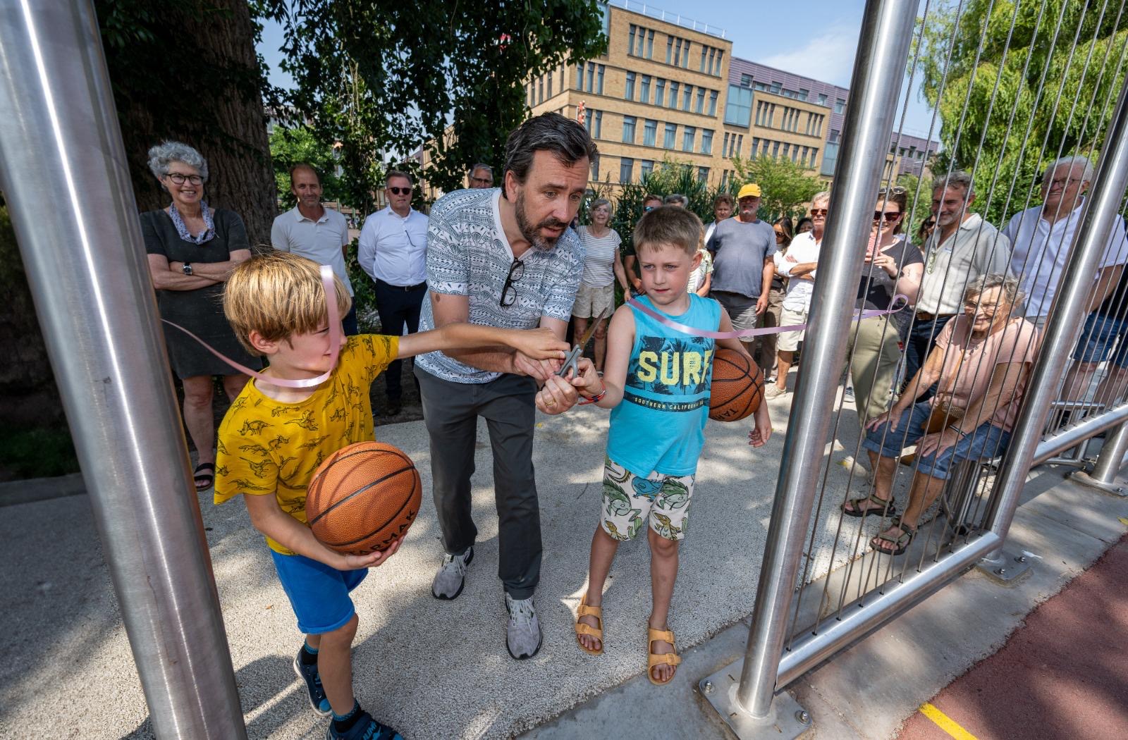 Zeeger Ernsting knipt samen met twee kinderen het lint door bij de opening van een nieuw basketbalveld