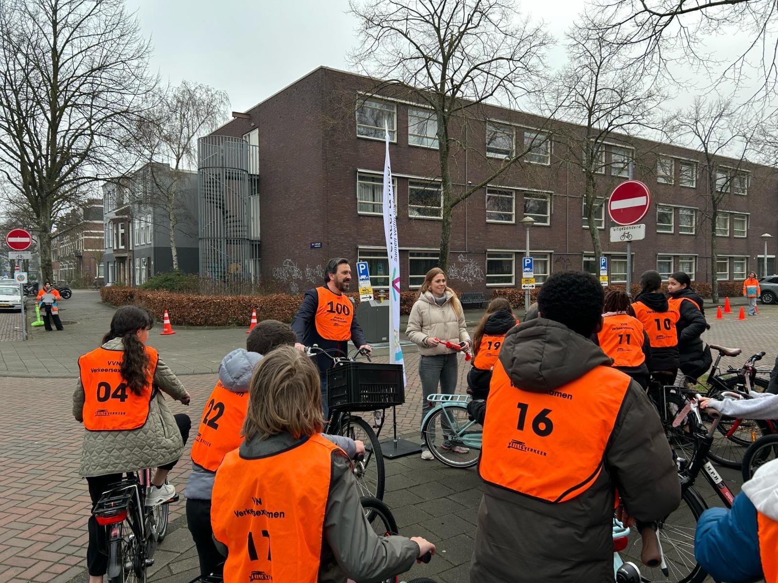 Zeeger Ernsting spreekt een groep kinderen toe die met fietsen en oranje hesjes klaarstaan voor een verkeersexamen